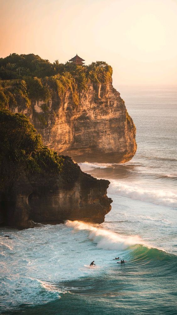 Uluwatu cliffs and temple at golden hour, with surfers below